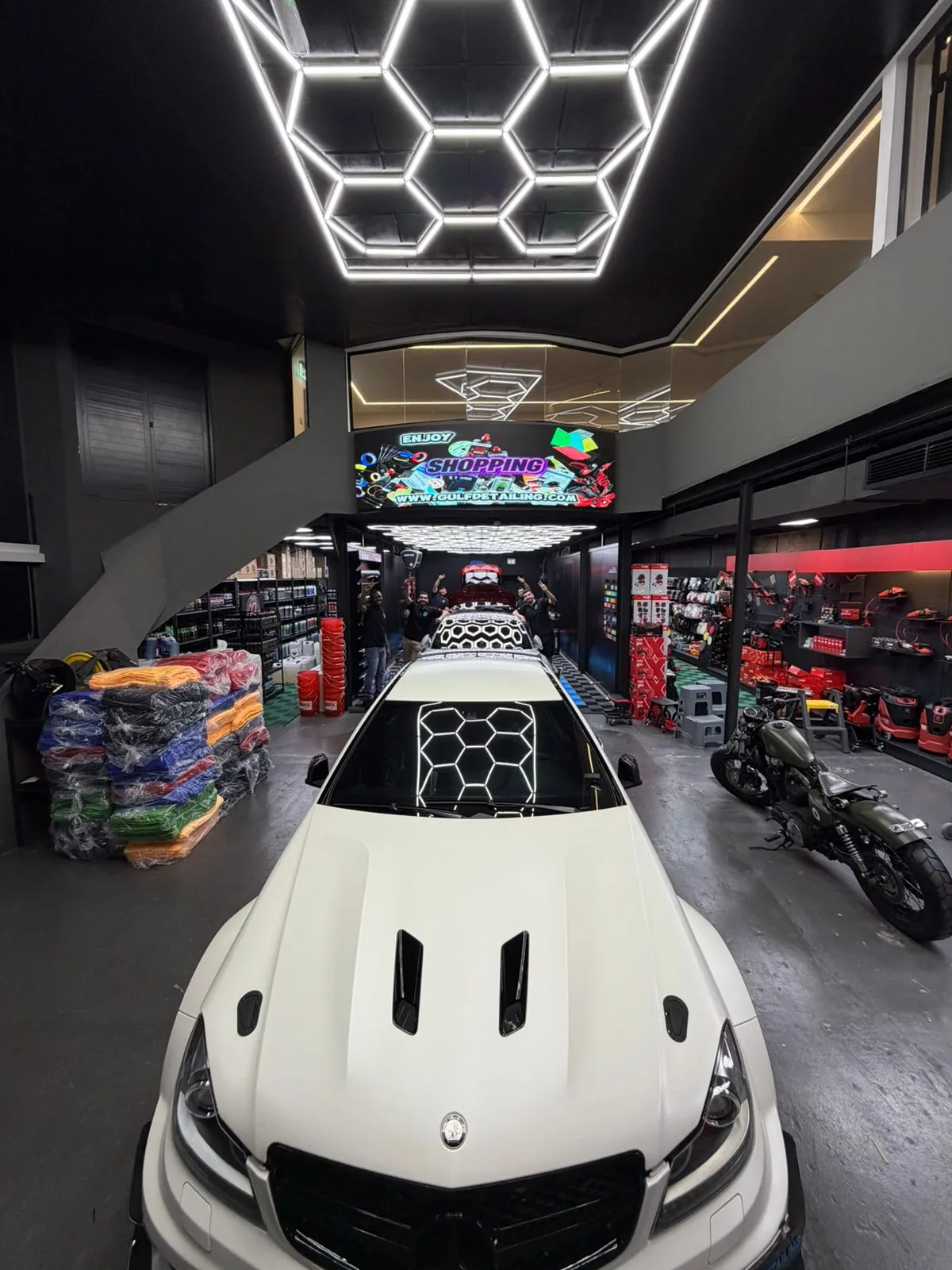 A matte-white performance car parked beneath hexagon lighting in the Gulf Detailing showroom