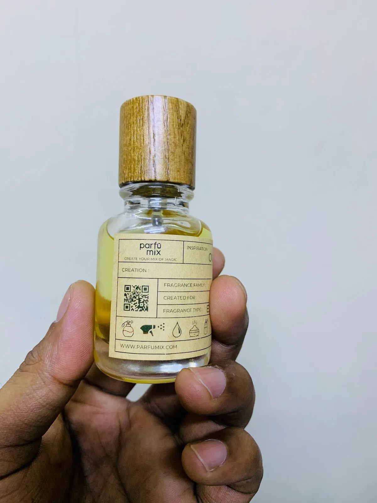 A hand holding a Parfumix oil bottle with a kraft information label