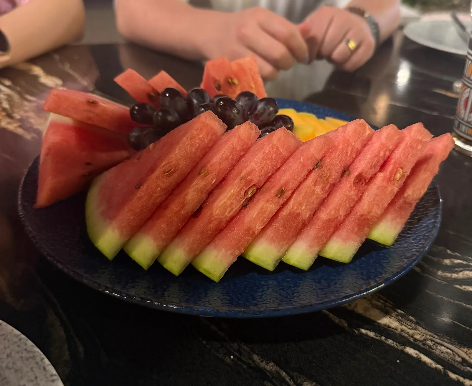 A platter of sliced watermelon and grapes on a blue plate