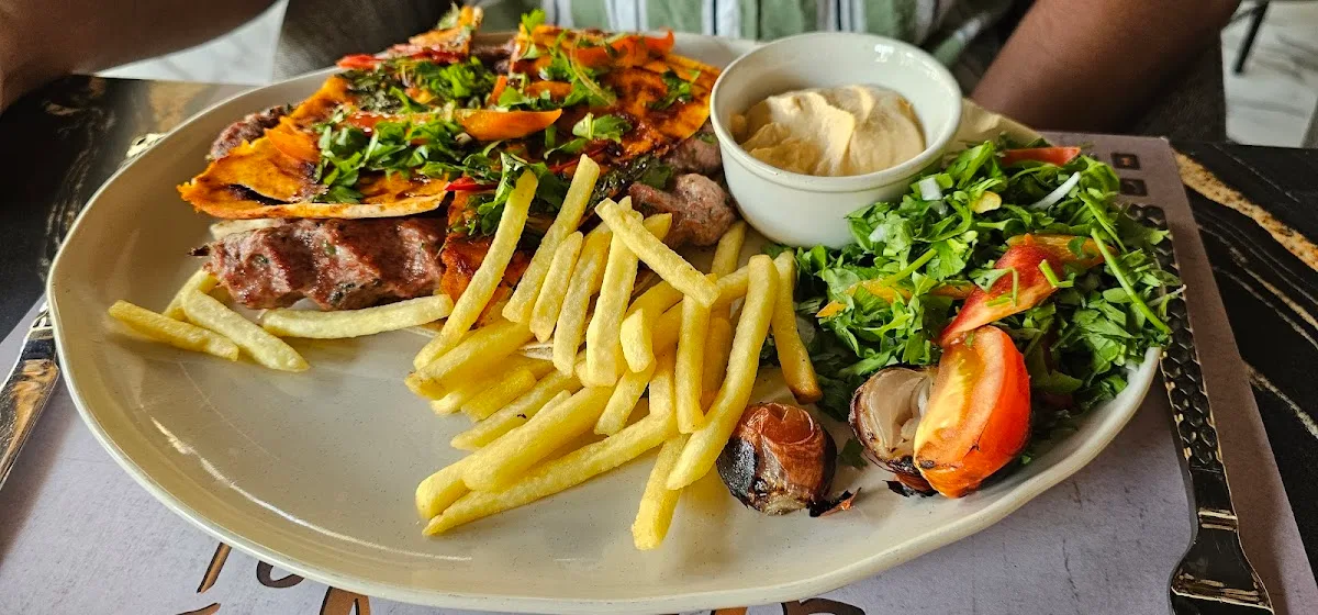 A mixed grill platter with grilled meats, flatbread, fries, fresh salad and a bowl of hummus