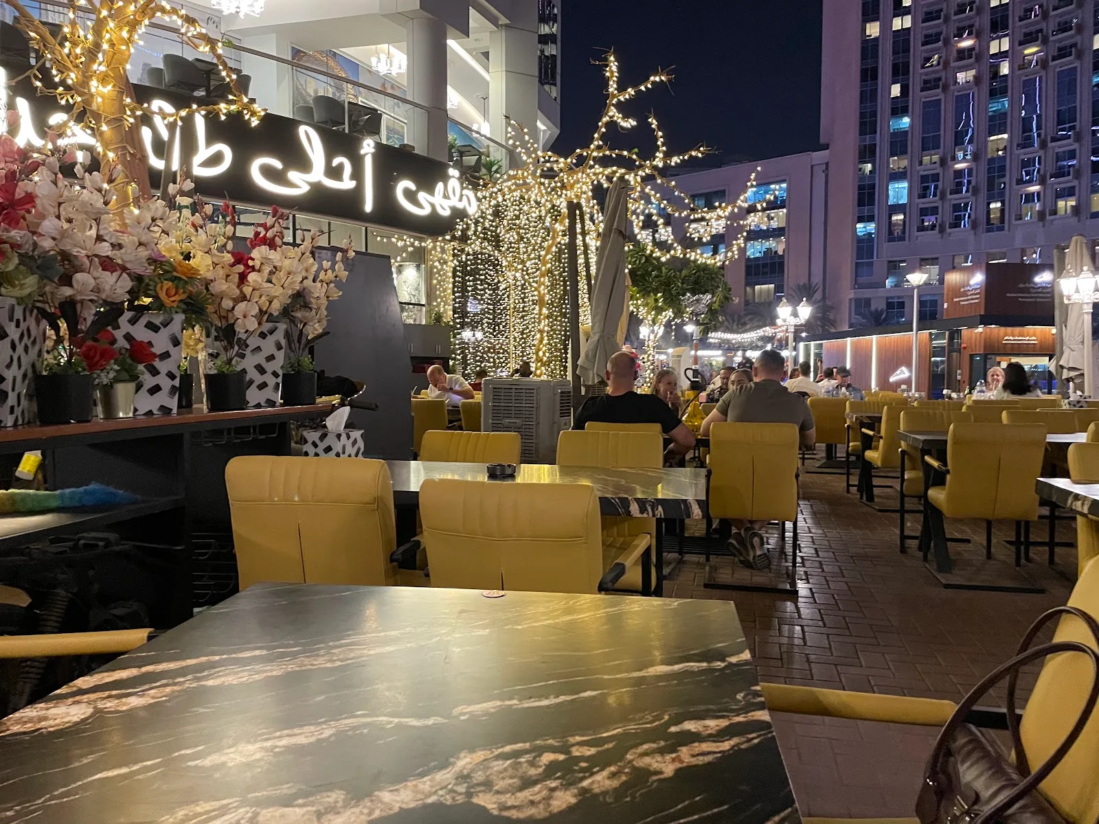 The night terrace with yellow lounge chairs, fairy-lit trees and an Arabic neon sign