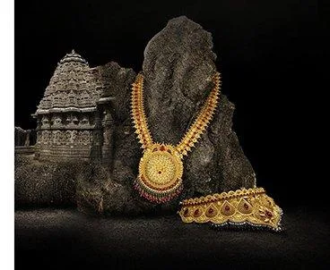 Handcrafted gold haaram necklace and choker displayed against dark stone and a carved temple backdrop