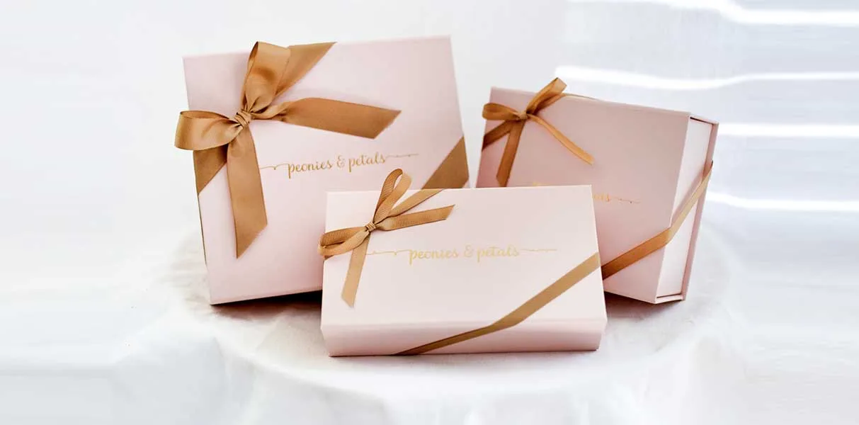 Three blush gift boxes tied with gold ribbon and the studio name