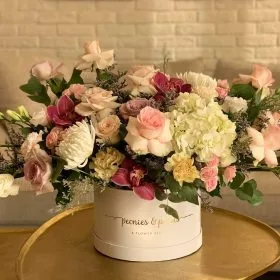 A pastel arrangement of roses and hydrangea presented in a round signature hatbox