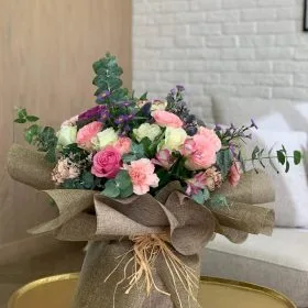 A rustic bouquet wrapped in burlap with mixed pink blooms