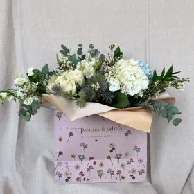 White and blue hydrangea bouquet in a branded paper bag