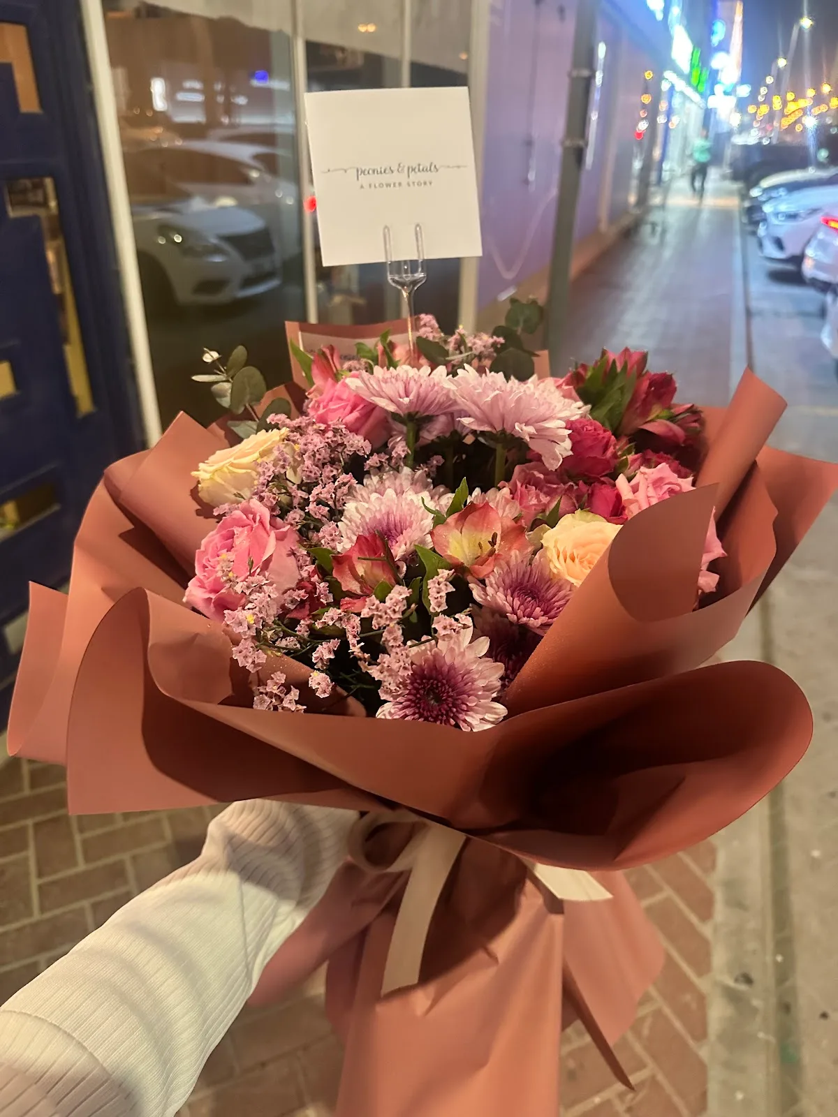 A hand-tied bouquet of roses, chrysanthemums and eucalyptus in mauve wrap