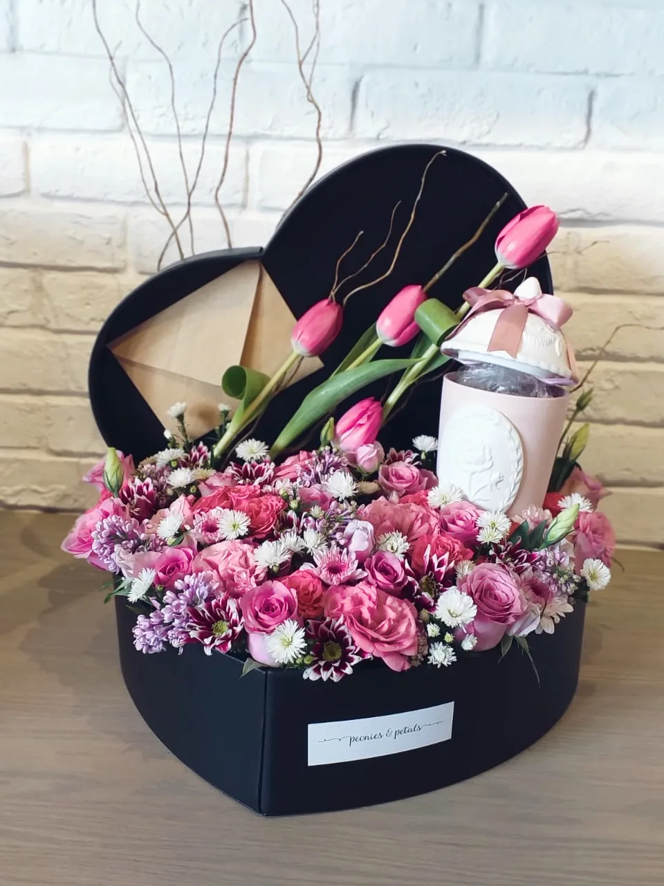 A black heart-shaped box filled with pink roses and tulips