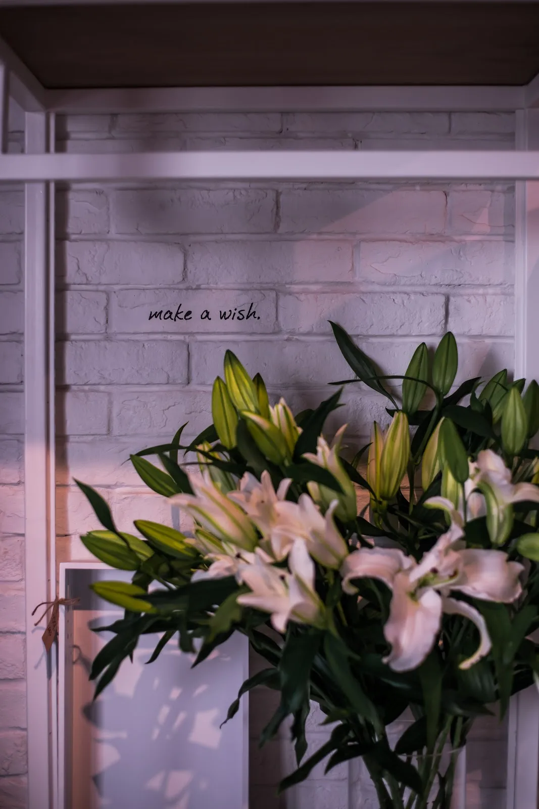 White lilies beside a hand-written 'make a wish' note on the studio wall