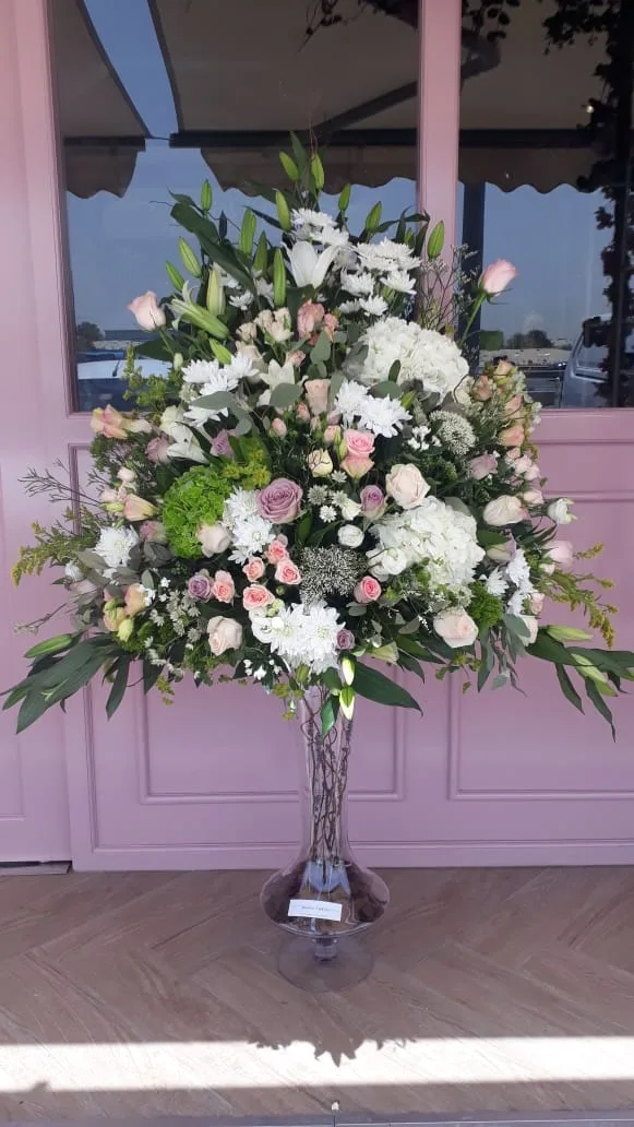 A tall pedestal arrangement of white and blush flowers displayed outside the studio