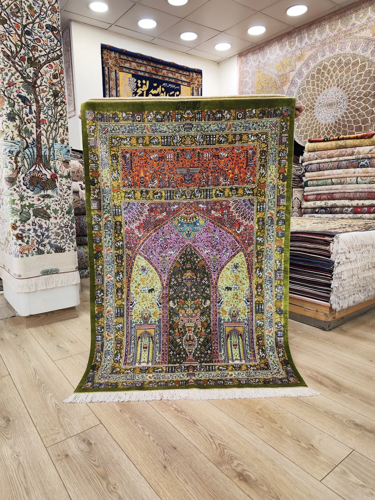 Green-bordered pictorial silk carpet held up in the showroom