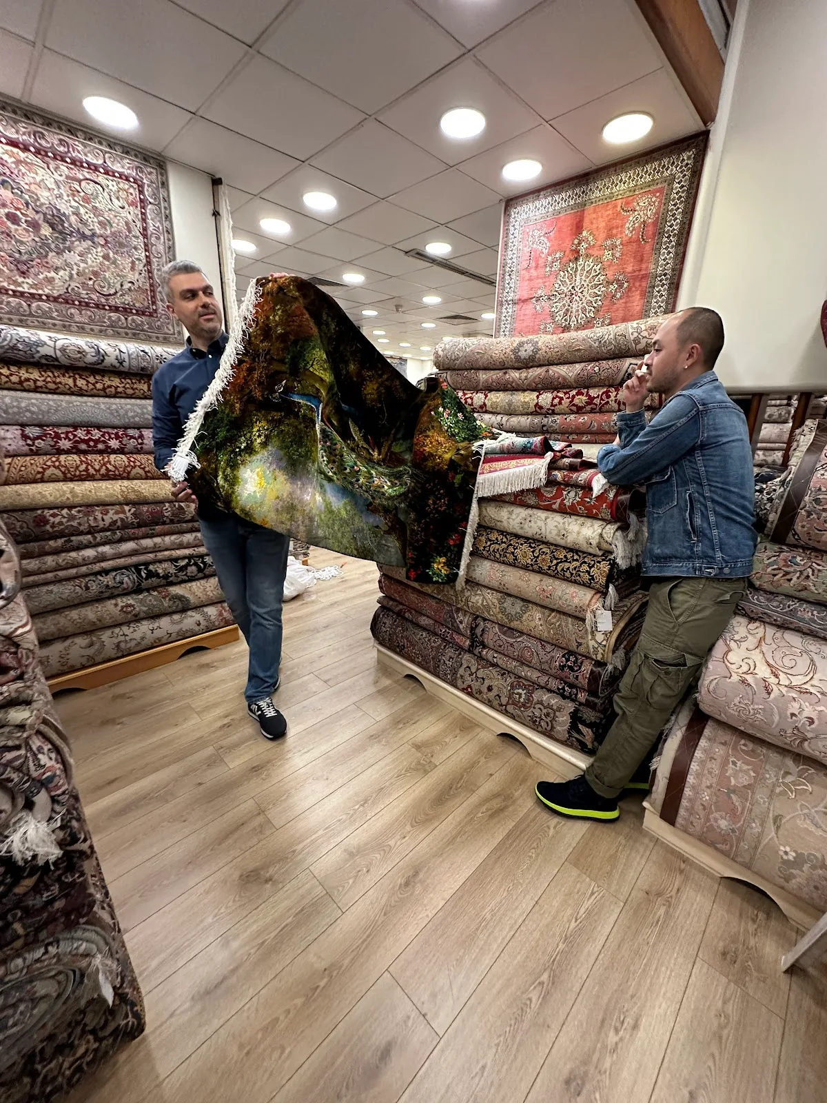 Two members of staff holding up a dark pictorial carpet