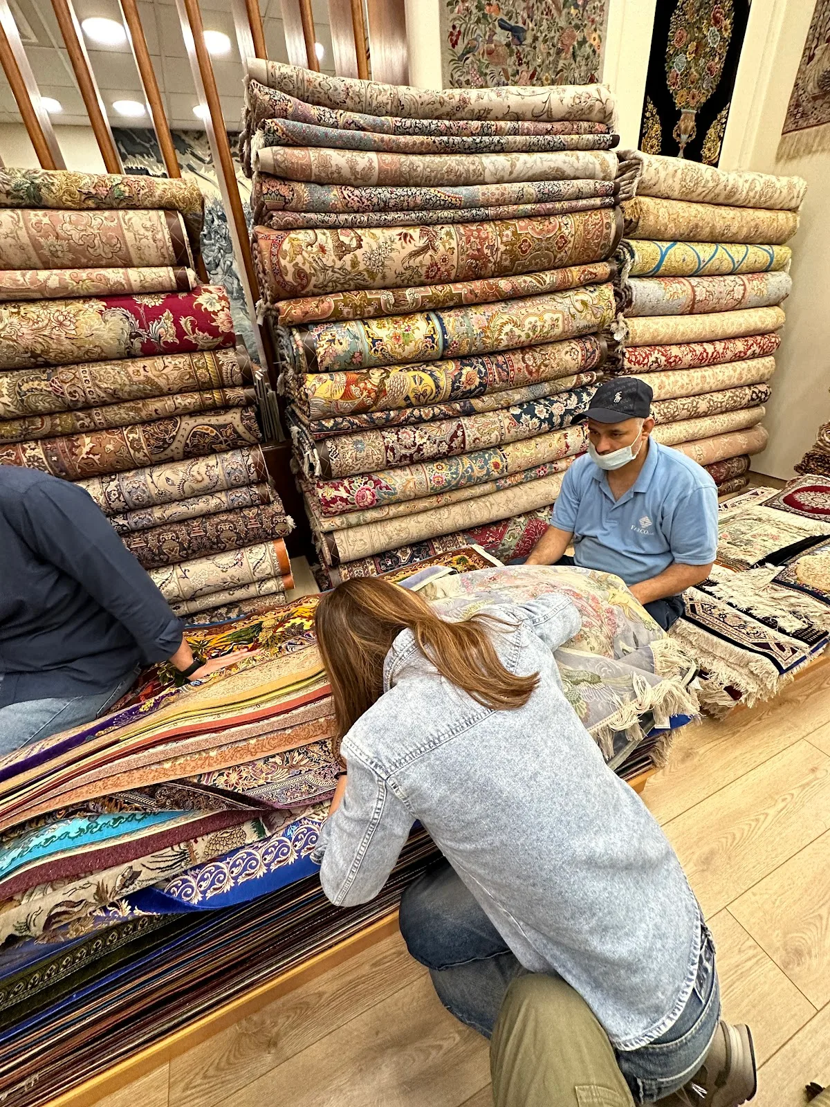 A customer and staff member examining a pile of fine carpets