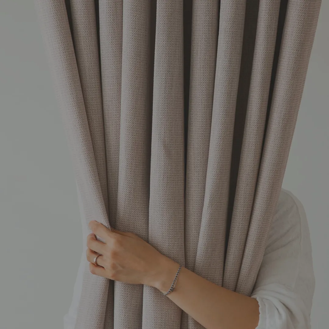 A hand drawing back a length of woven curtain fabric
