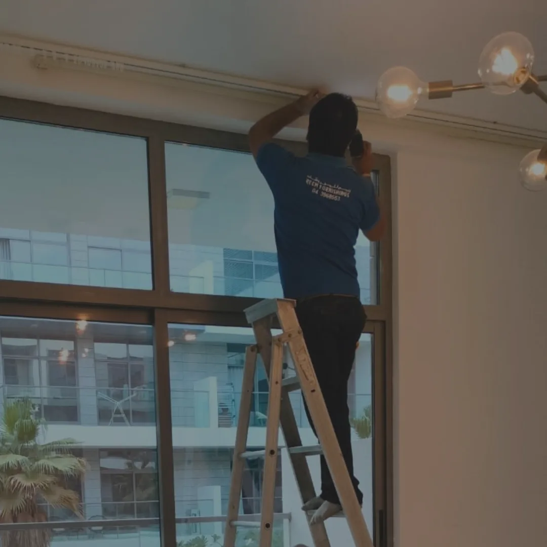 A Reem Furnishings fitter on a ladder installing a curtain track at a Dubai apartment window