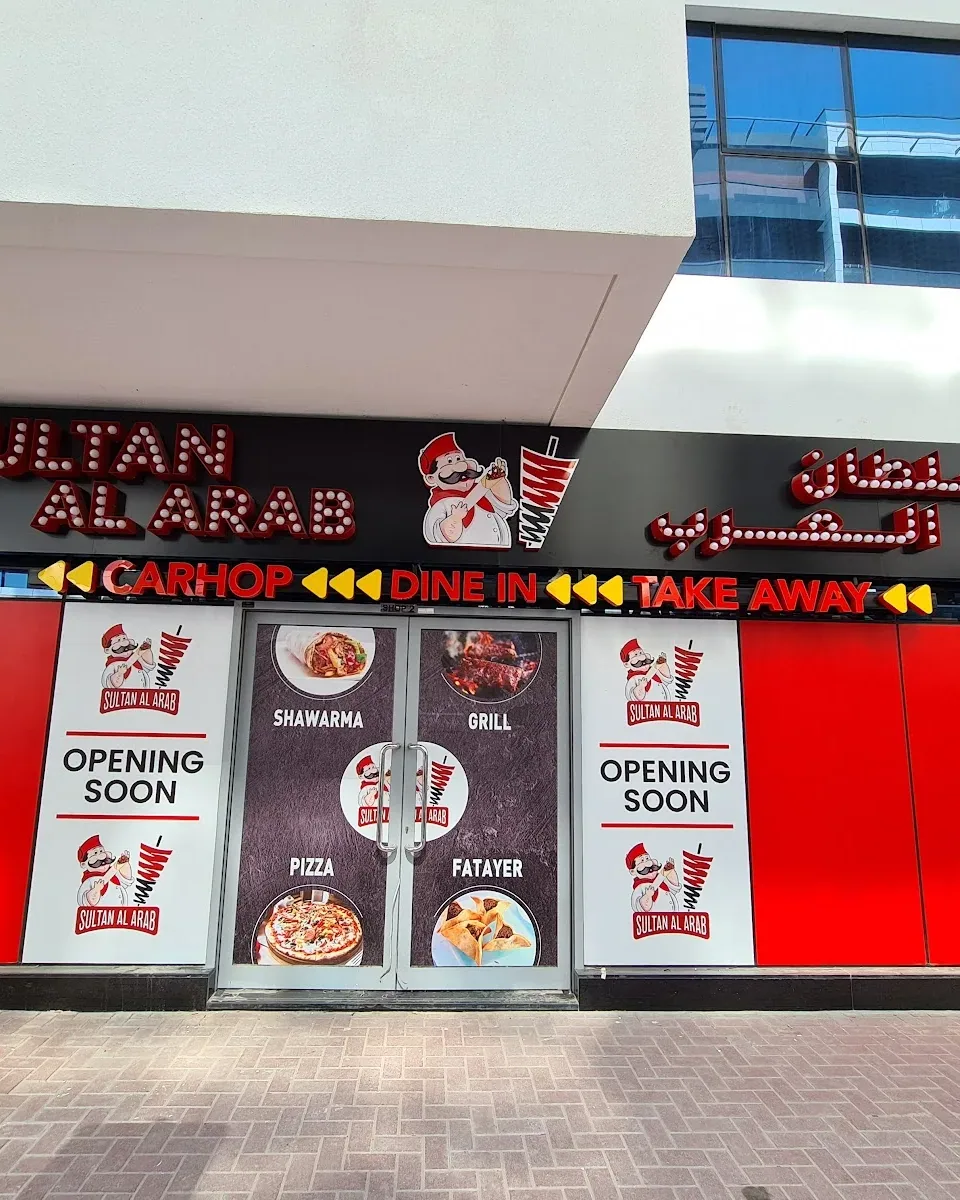 The Sultan Al Arab shopfront in Al Barsha, Dubai — illuminated red sign with the chef mascot above a glass door showing the shawarma, grill, pizza and fatayer menu
