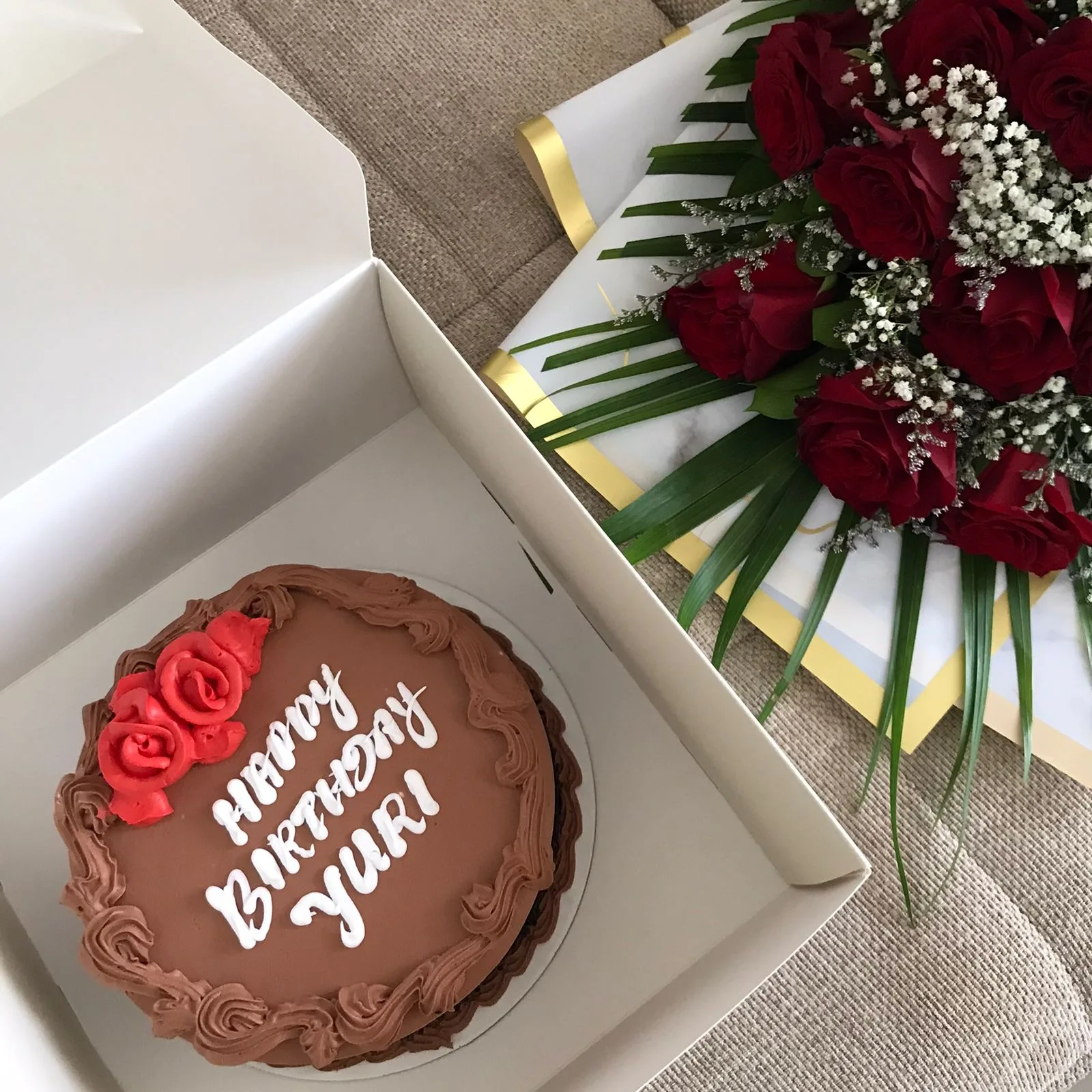 Chocolate birthday cake in a box beside a bouquet of red roses, ready to gift