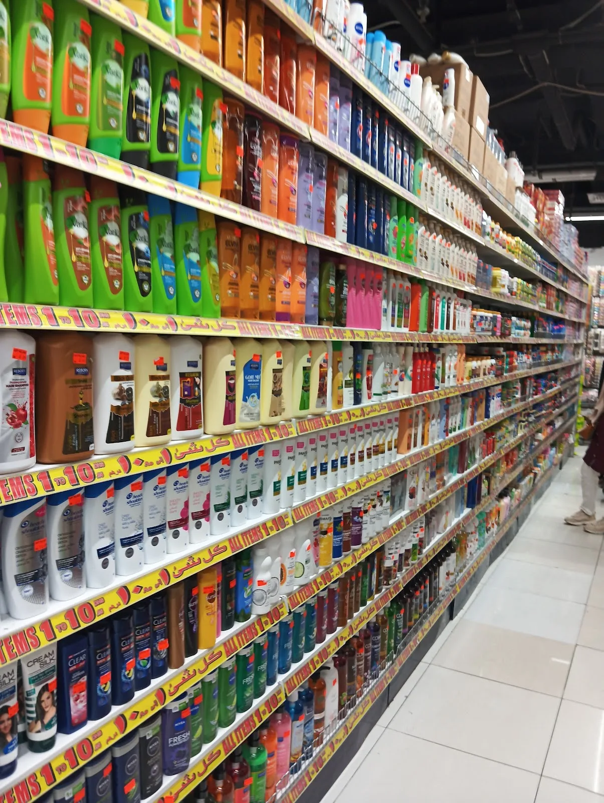 Long aisle of shampoo, soap and toiletries with 1 to 10 AED shelf strips at Gifts Village