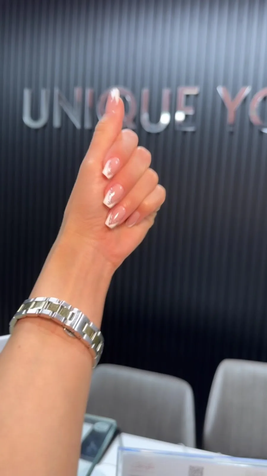 A guest at Unique You Al Barsha showing fresh chrome French manicure in front of the studio's Unique You signage