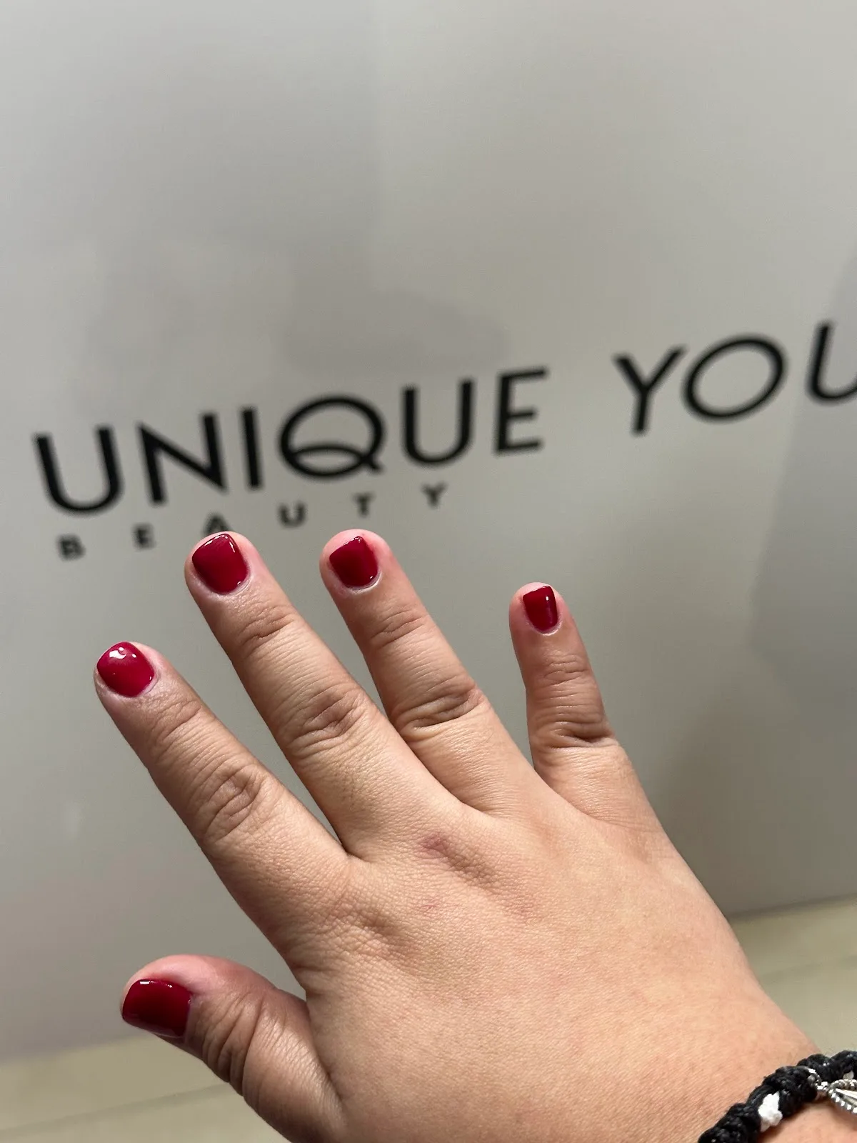 Red manicure photographed in front of the Unique You Beauty wall signage