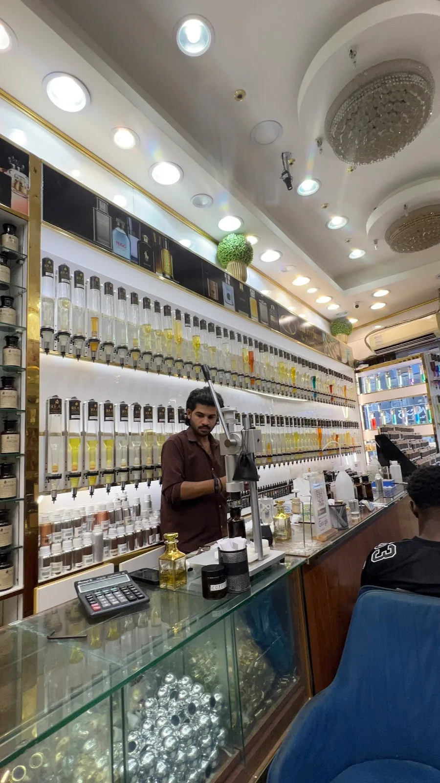A Real Perfumes perfumer blending fragrance oils at the wall of dispensers behind the counter in Deira