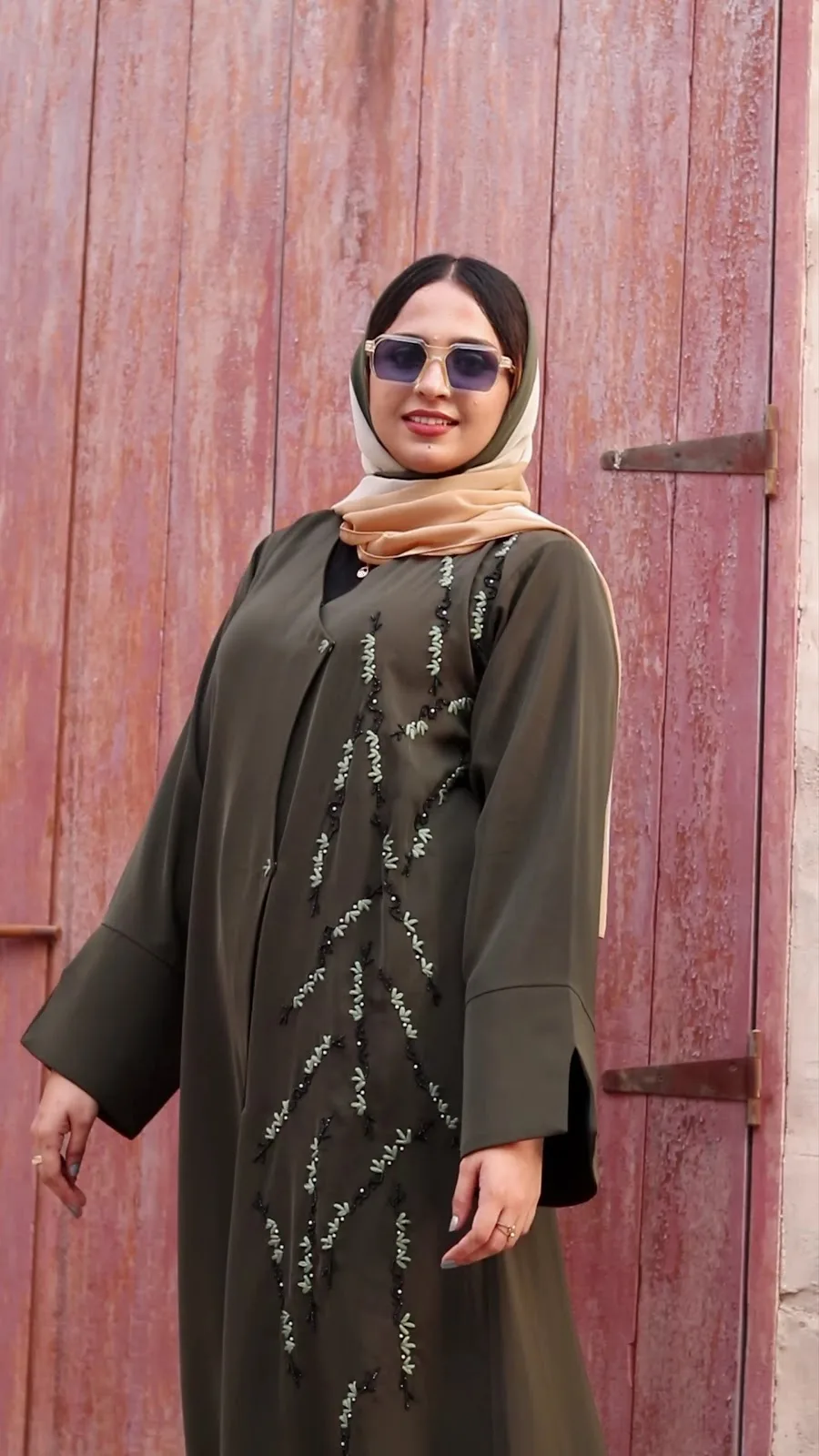 Model in an olive abaya with leaf beadwork against a red door