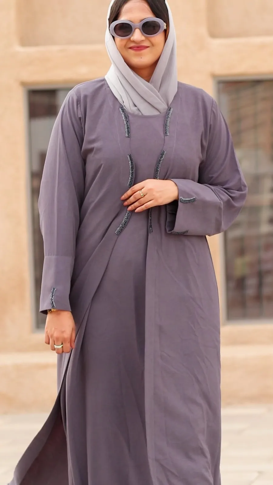 Model wearing a lilac abaya with beaded trim against warm Deira stonework