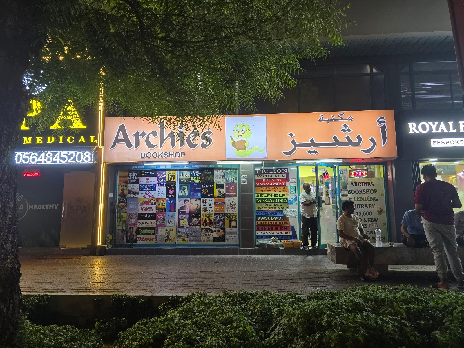 The Archies Bookshop storefront at night on 11th Street, Al Karama, with its lit orange sign and window full of books