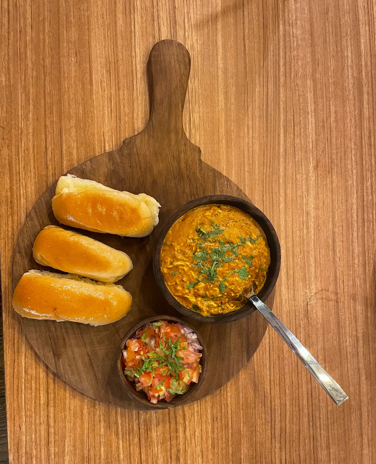 Pav bhaji served on a round wooden board — buttered pav, rich masala and fresh chopped salad