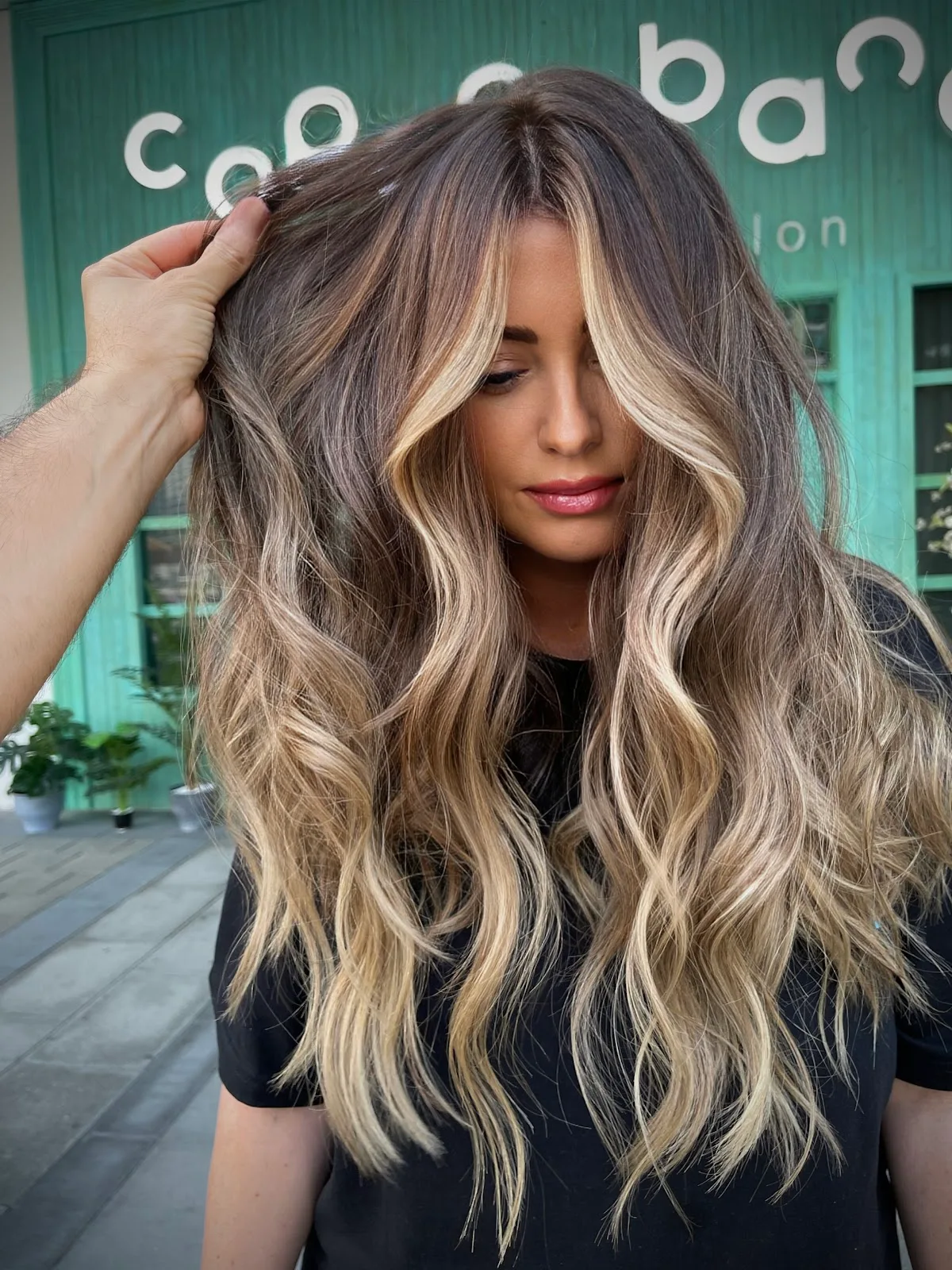 A client showing long honey balayage waves in front of Copacabana's turquoise storefront in Business Bay