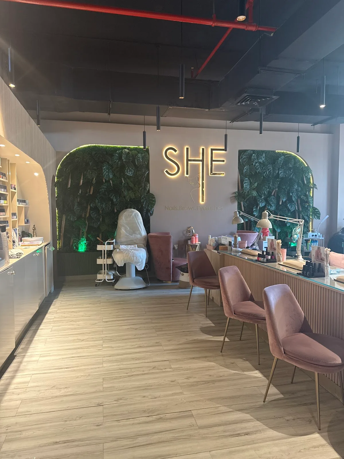 SHE Beauty Salon reception with the gold SHE sign and pink chairs along the manicure bar