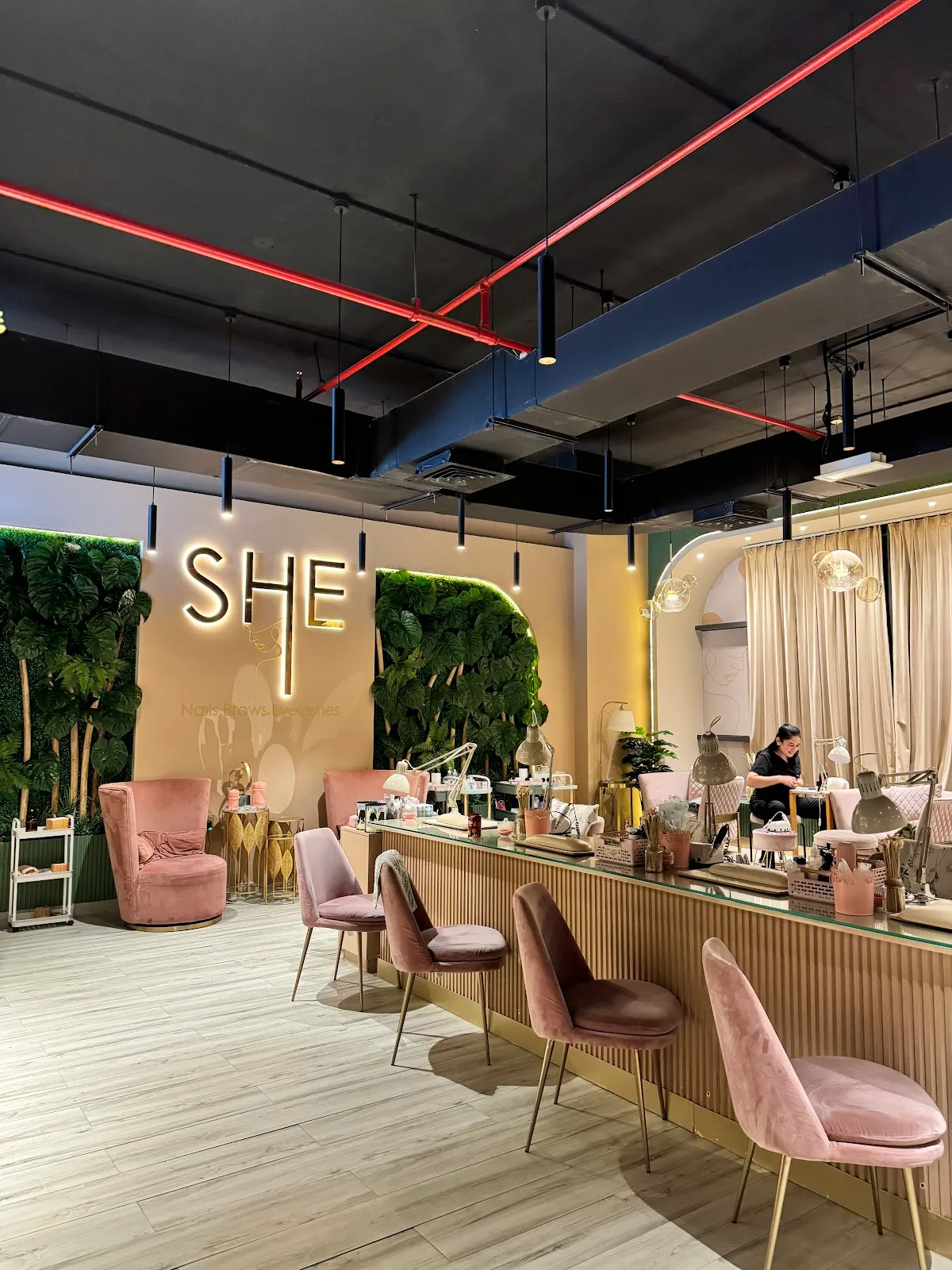Interior of SHE Beauty Salon showing the gold SHE sign, blush velvet chairs and green plant walls