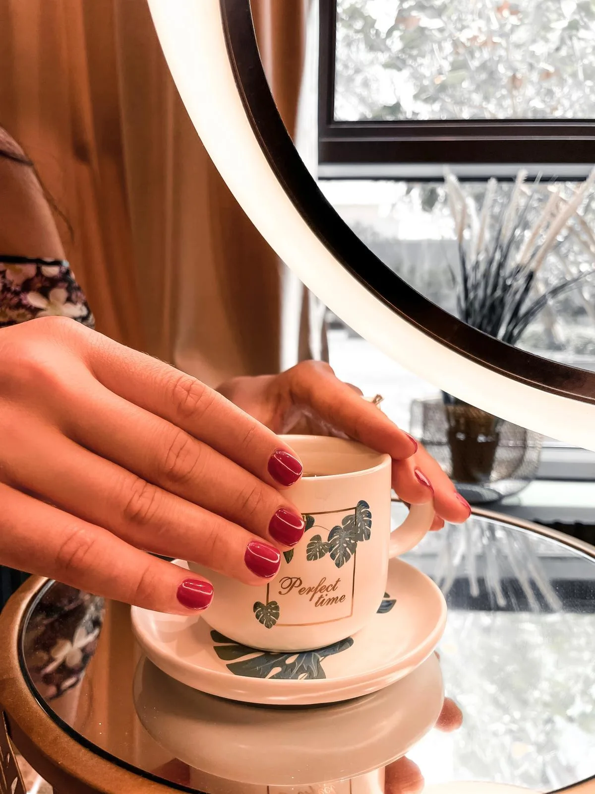 Glossy red manicure holding a botanical mug