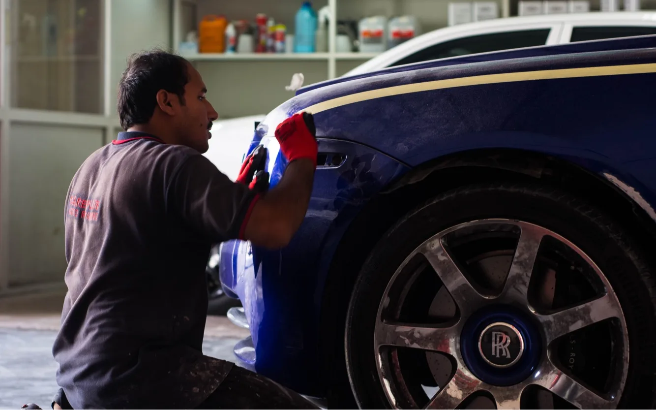 Care Plus technician hand-polishing the paintwork of a blue Rolls-Royce in the Al Quoz workshop