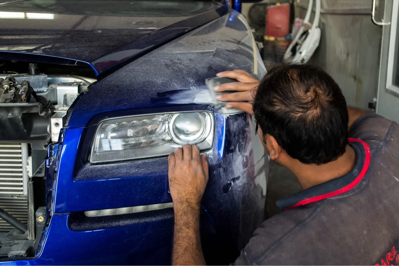 Care Plus technician carefully sanding and refinishing the front panel of a blue Rolls-Royce