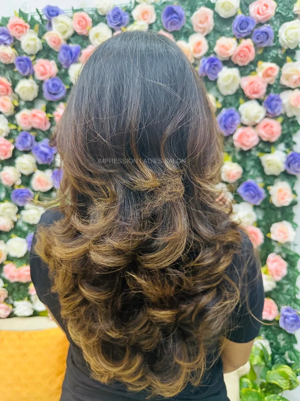 Layered wavy blow-dry styled against the salon's signature flower wall at Impression Ladies Salon