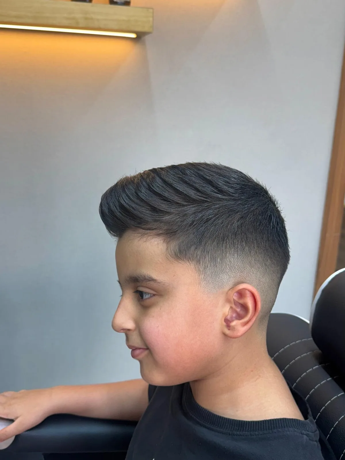 Young boy with a neat textured haircut and light fade in the barber chair