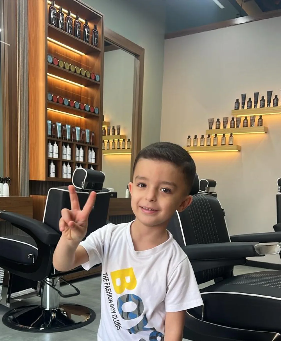 Smiling boy with a fresh haircut throwing a peace sign in the barber chair