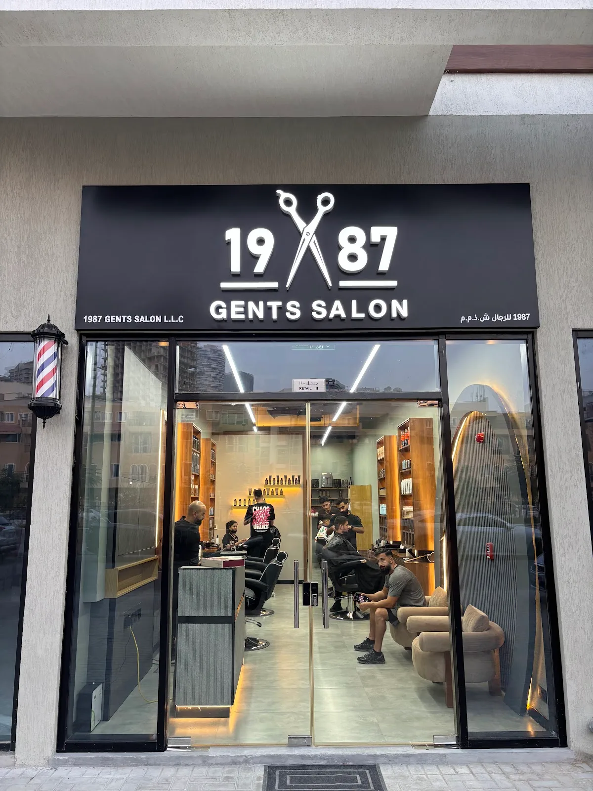 Storefront of 1987 Gents Salon in Jumeirah Village Circle, Dubai, with the lit scissors logo sign and a barber pole