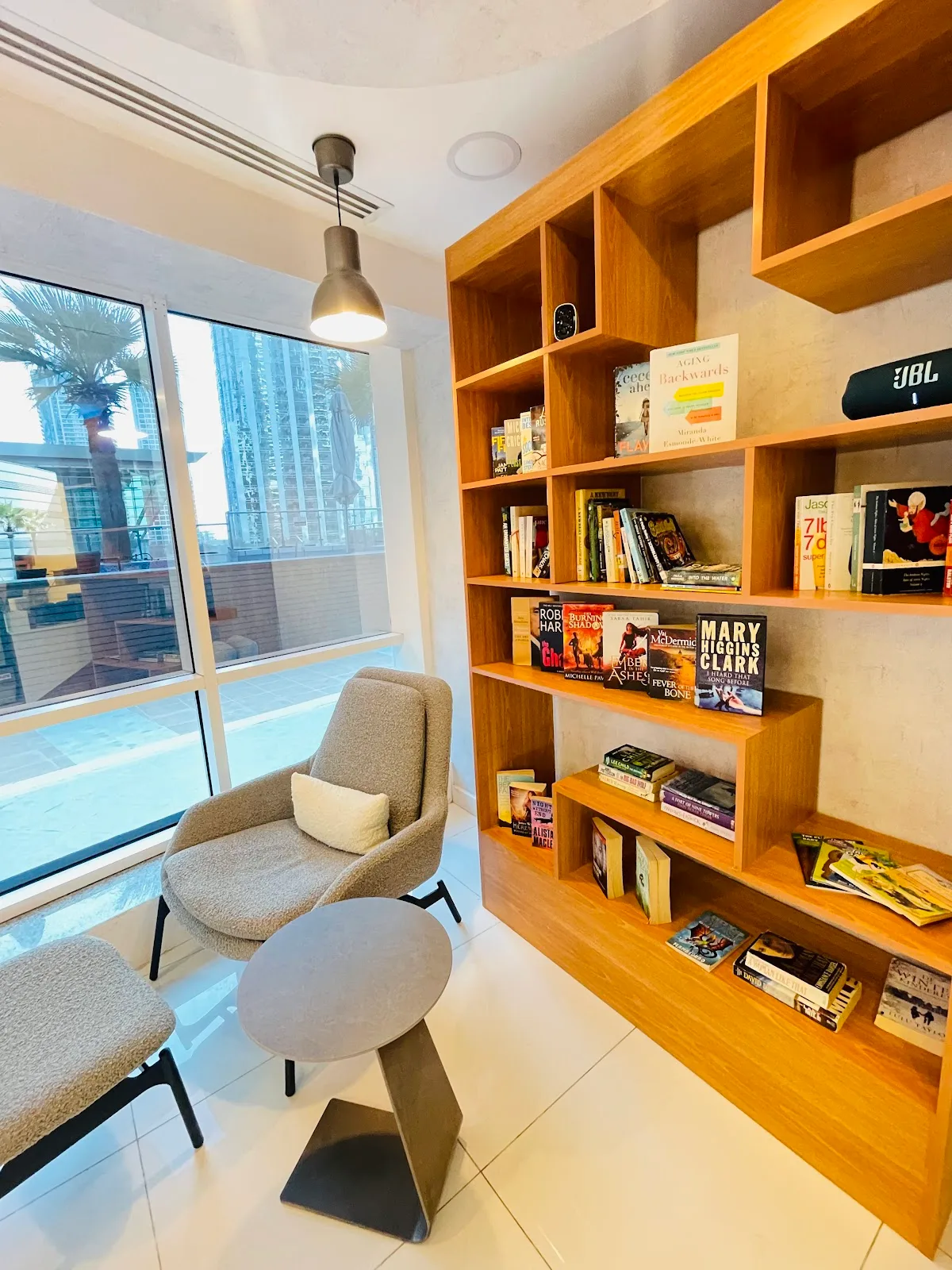 Reading corner with a bouclé armchair, full bookshelf and tower views over JLT