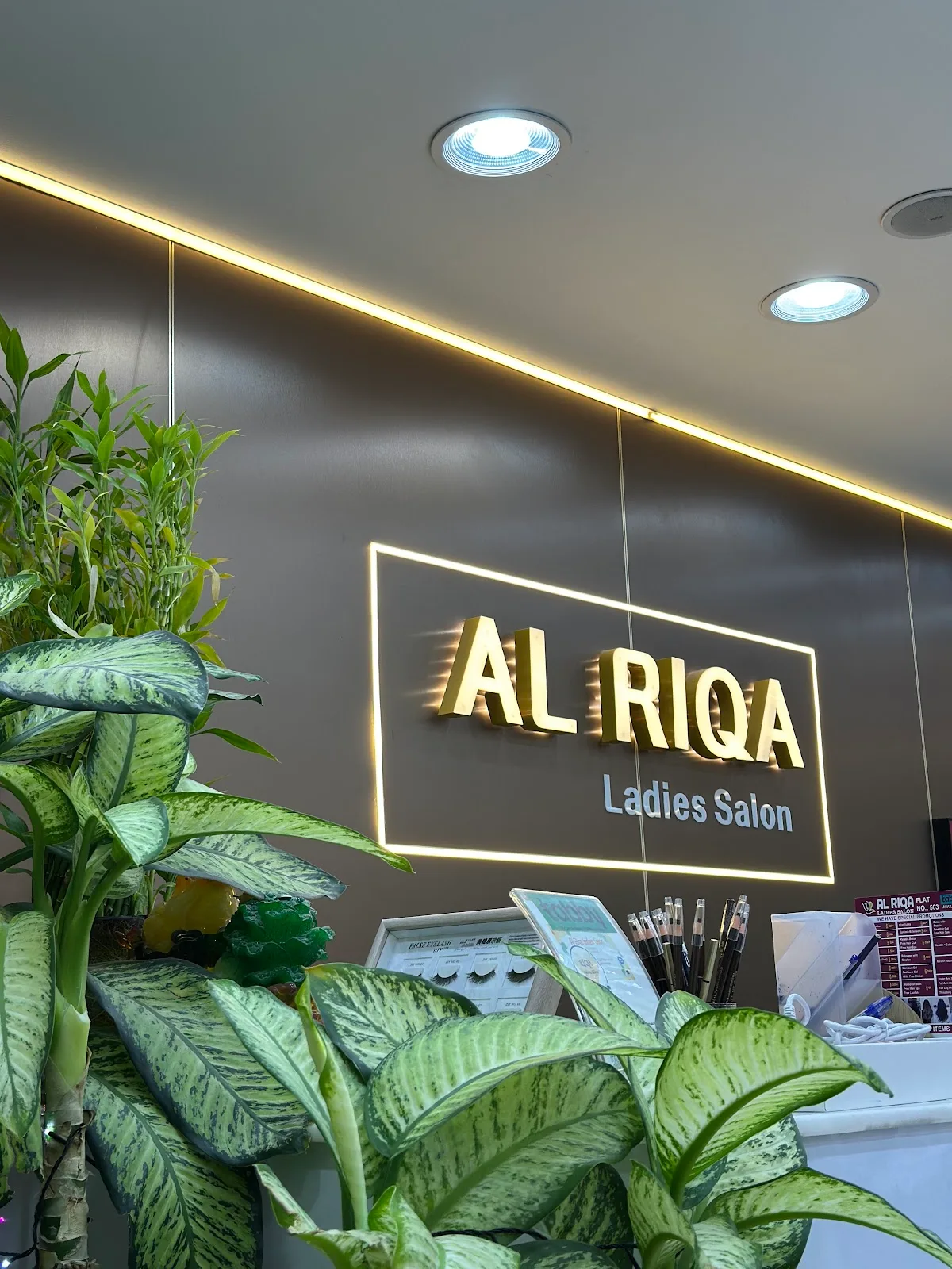 The gold backlit Al Riqa Ladies Salon sign surrounded by lush green plants at reception