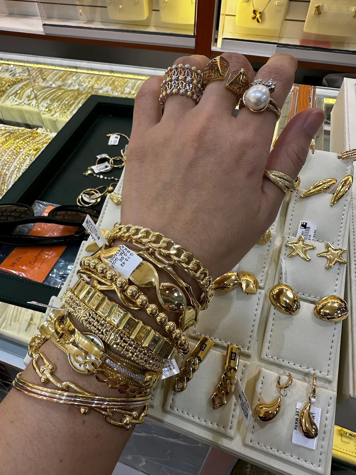 A hand stacked with 22K gold bangles and rings over a tray of gold pieces