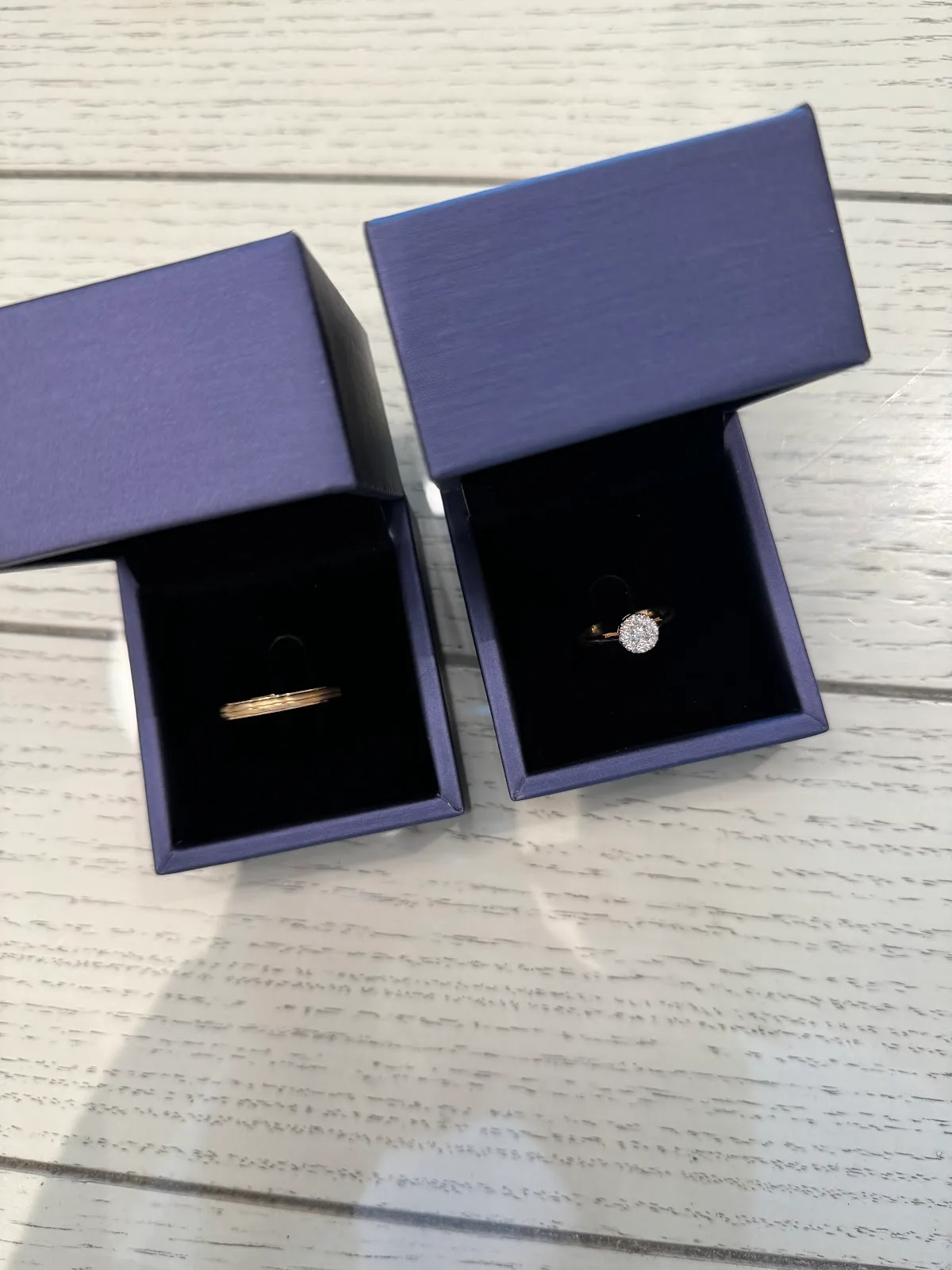 A diamond ring and a gold band shown in navy presentation boxes
