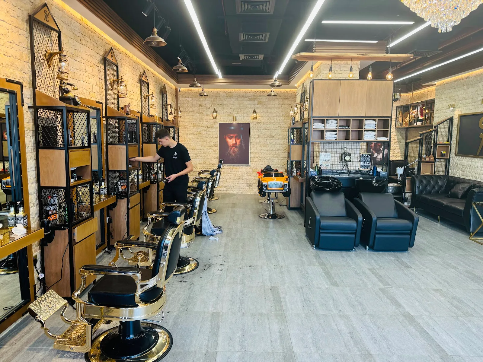 Wide view of the Shave Cave interior — gold barber chairs, exposed brick, vintage lanterns and chandeliers