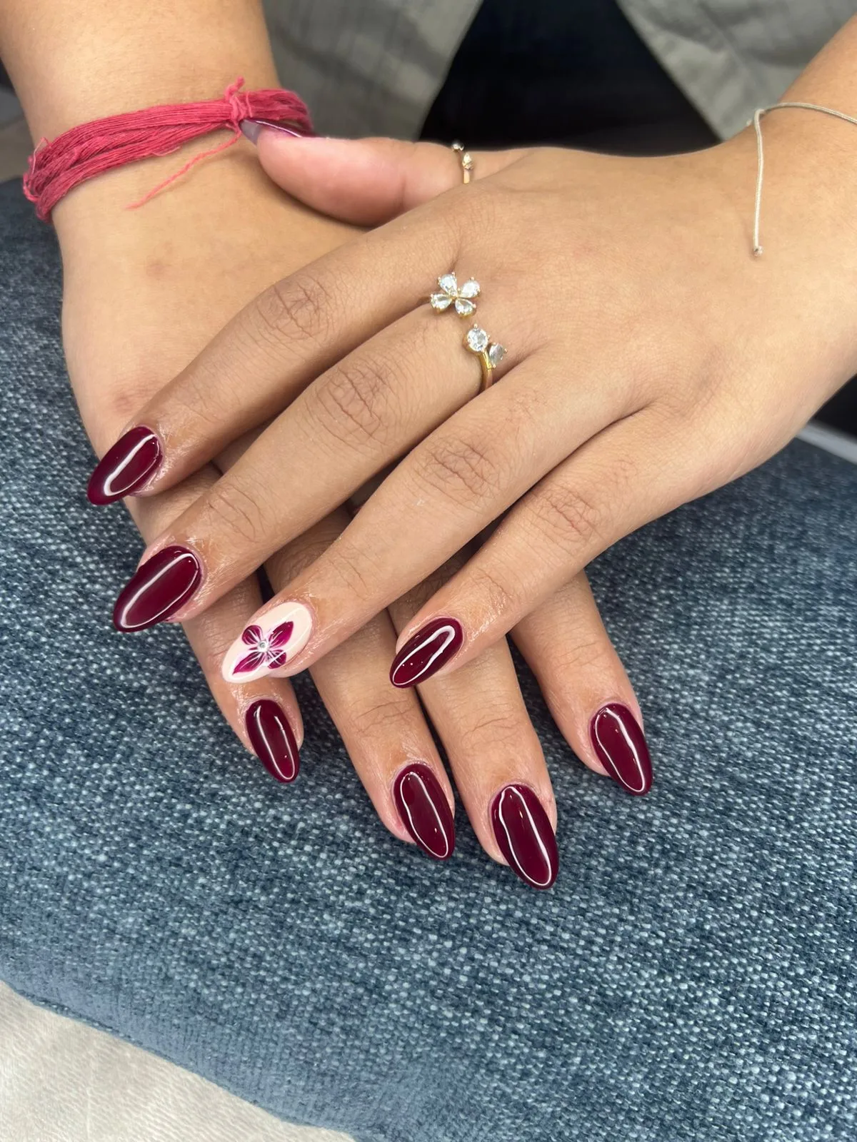Deep burgundy almond gel manicure with a hand-painted floral accent nail at N Dot K Beauty Lounge