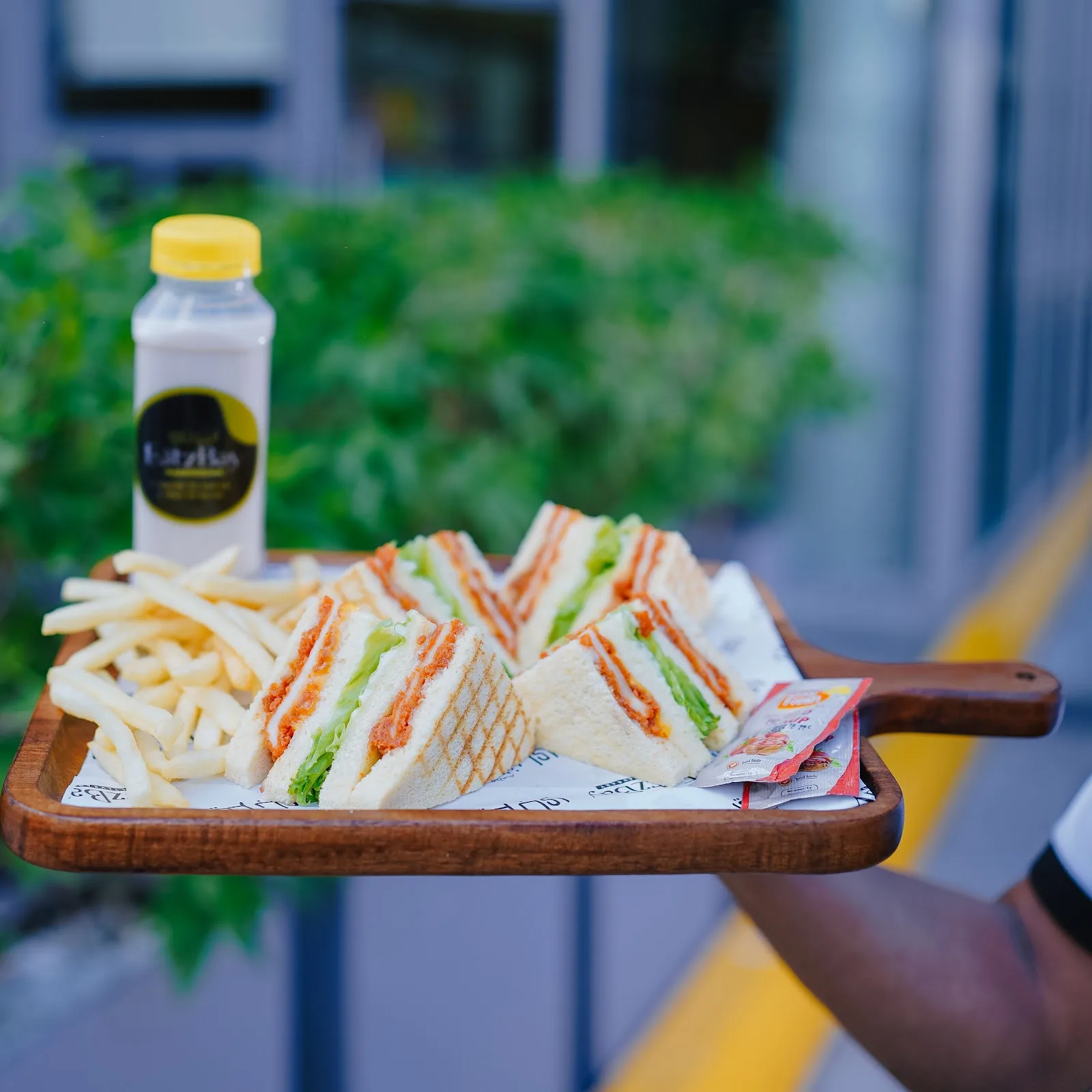 Toasted club sandwich quarters with fries and a chilled Eatz Bay drink served on a wooden board