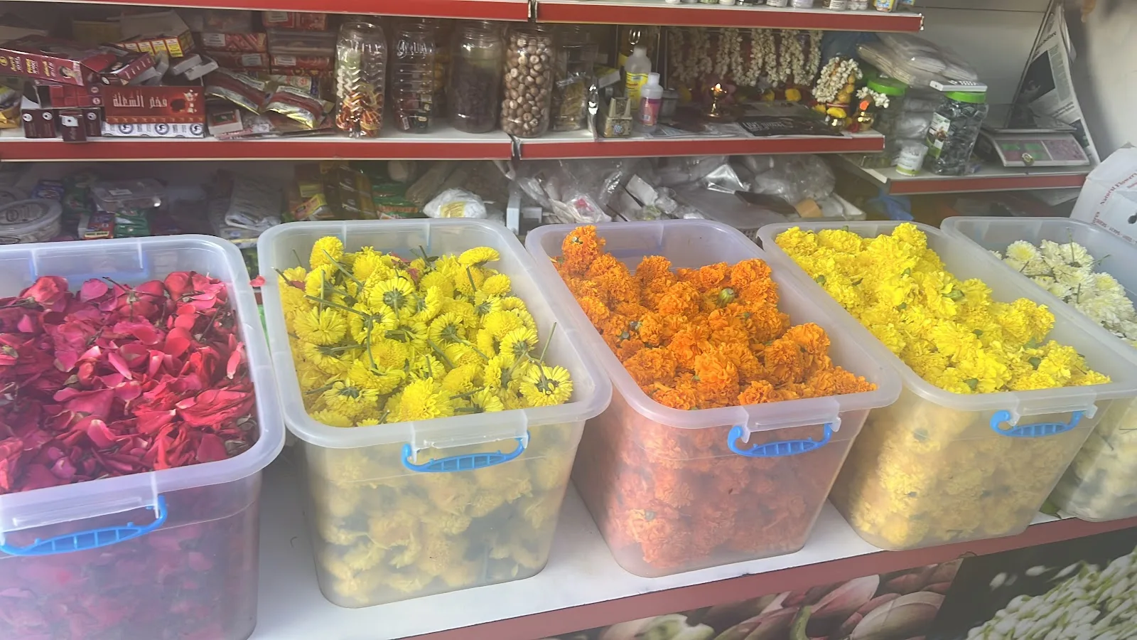 Bins of loose flowers at Perumal Flowers — red rose petals, yellow chrysanthemum, orange marigold and white jasmine sold by weight.