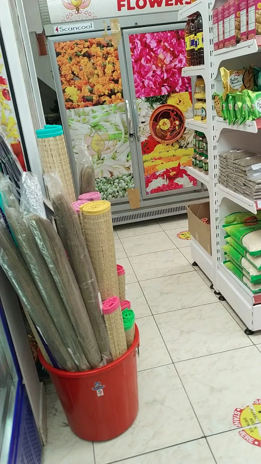 The interior of Perumal Flowers with a flower display fridge and shelves of grocery and pooja items.