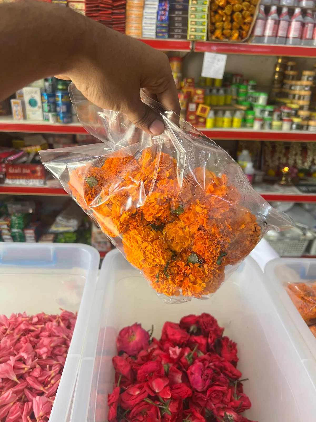 A clear bag of fresh orange marigold flowers held above bins of red rose petals.