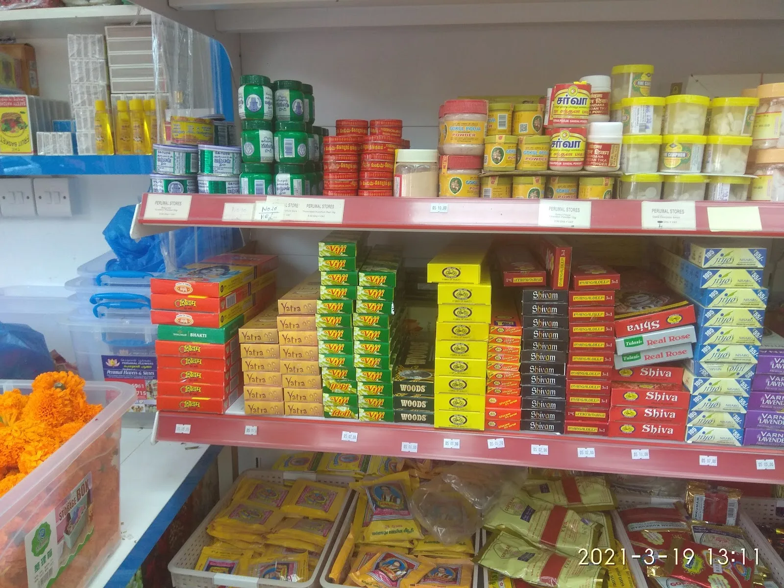 Shelves of pooja supplies at Perumal Flowers — incense, dhoop, sambrani, kumkum, sandal powder and camphor.